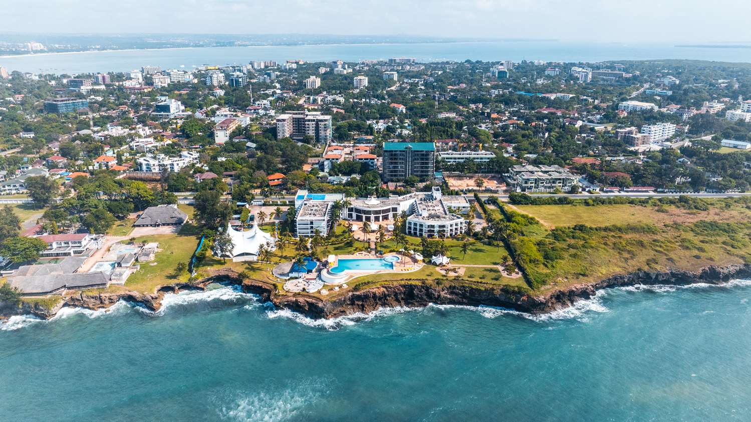 Aerial view of a coastal resort with buildings, pools, and ocean