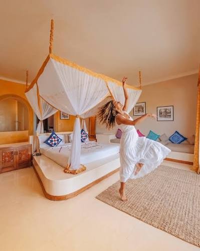 A woman in a white dress dancing in a hotel room with a canopy bed