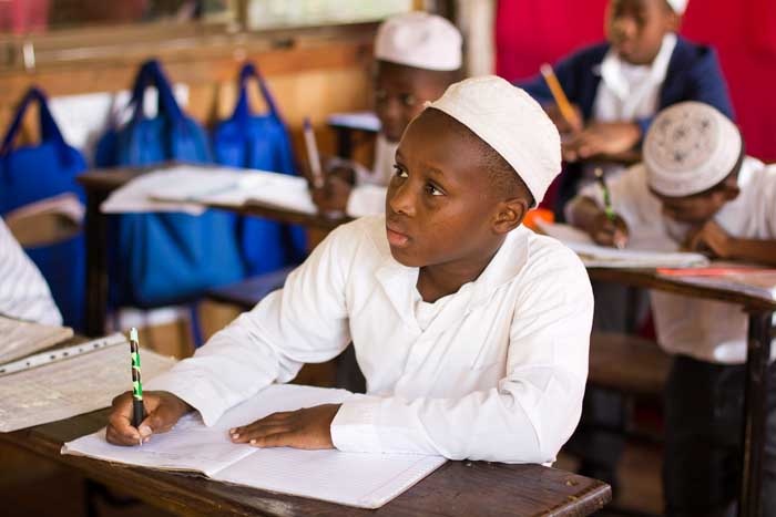 A young Zanzibari schoolboy writing in his notebook in a classroom